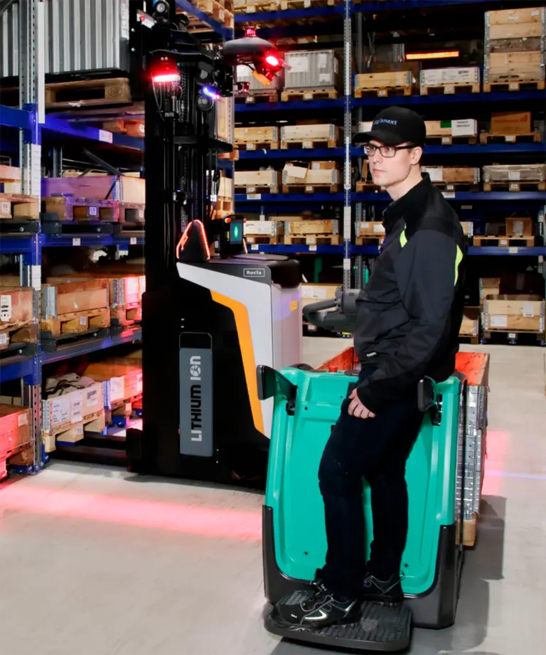 Medarbejder i Logisnext Denmark-kasket kører palleløfter forbi Rocla AGV-truck med sikkerhedsprojektion