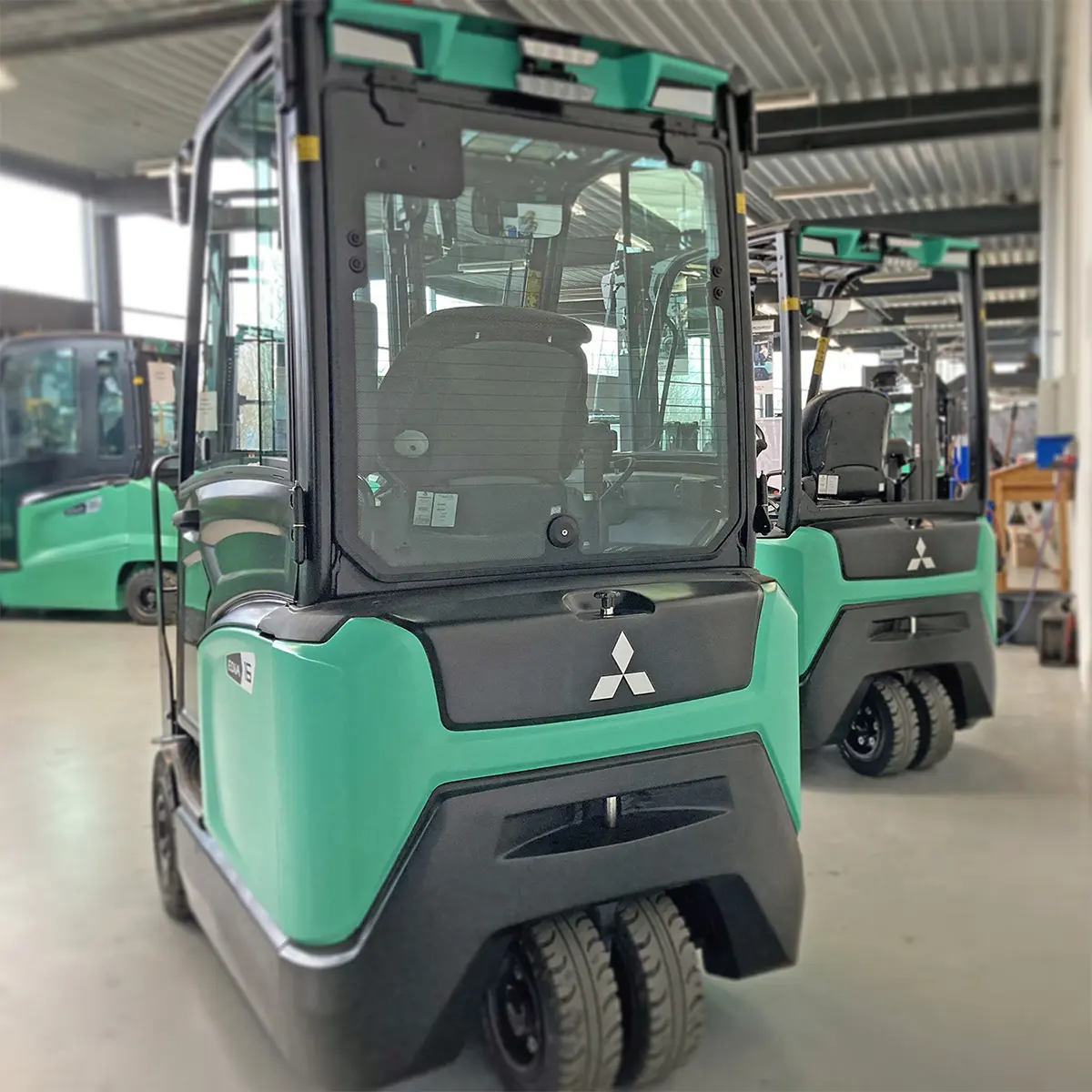 Flera Mitsubishi Edia elektriska motviktstruckar med Mitsubishi-logotyp uppställda bakifrån i produktionshall – Logisnext