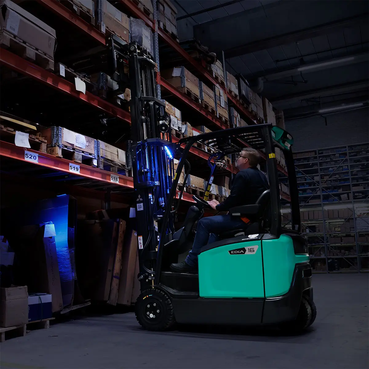EDiA 16-gaffeltruck fra Logisnext Denmark med blå sikkerhedslys kører i dæmpet belyst lager