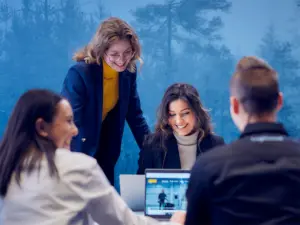 Kvinder samarbejder smilende omkring bærbar computer i moderne mødelokale hos Loginext