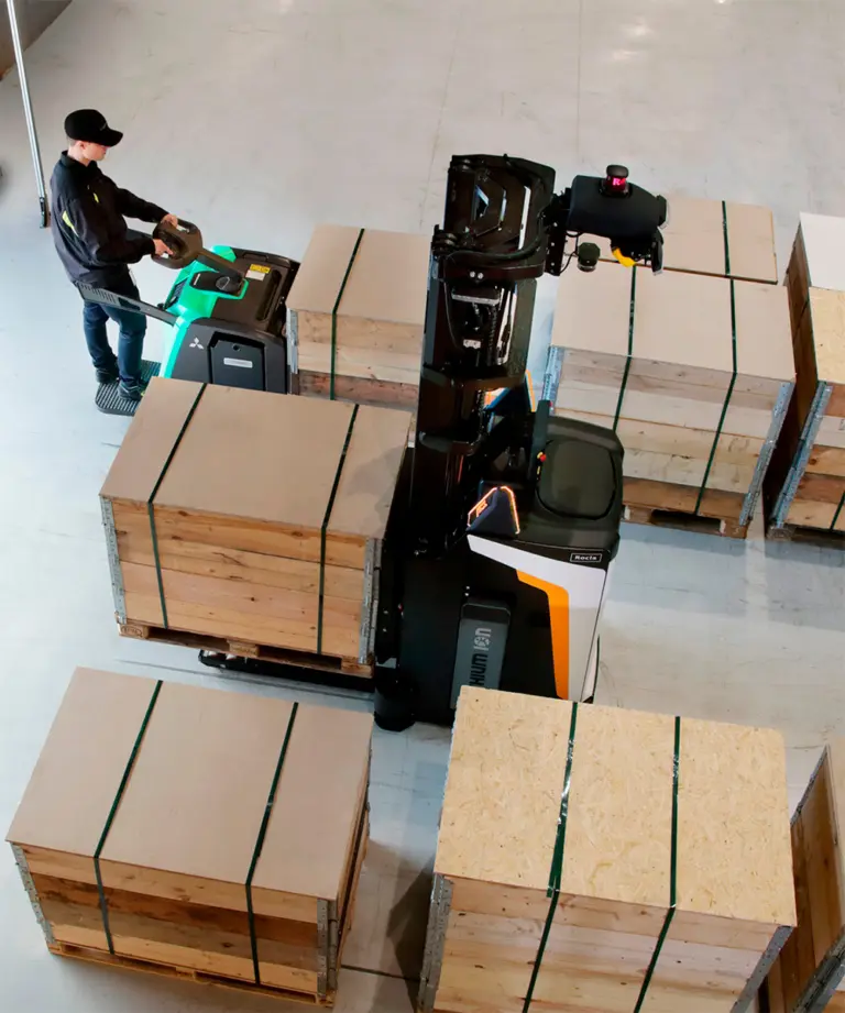 Fugleperspektiv af Rocla AGV-truck fra Logisnext Denmark der håndterer paller mellem medarbejder og lagerkasser